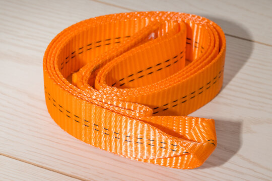 Close-up of an orange lifting strap with reinforced stitching, used for industrial and cargo applications.