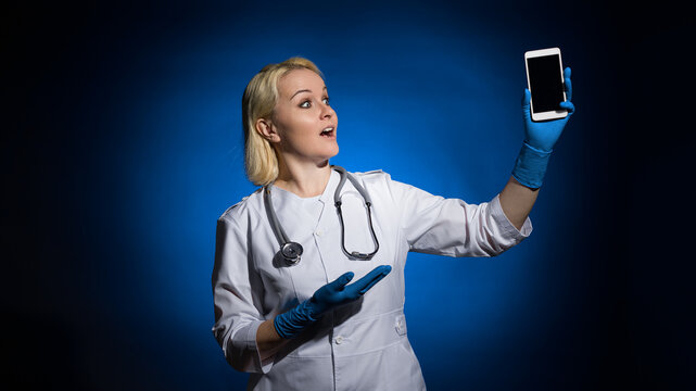 a female therapist in a white coat looks in surprise at a mobile phone in her hand on a dark background