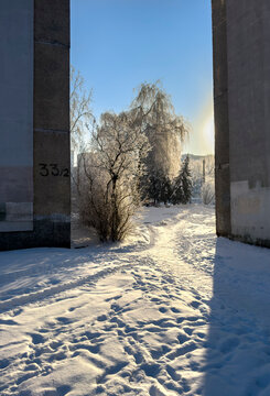 A winter city courtyard with gray multi-story panel buildings (Khrushchev-era or Brezhnev-era buildings) covered in a thin layer of snow and frost, under a bright blue sky. 