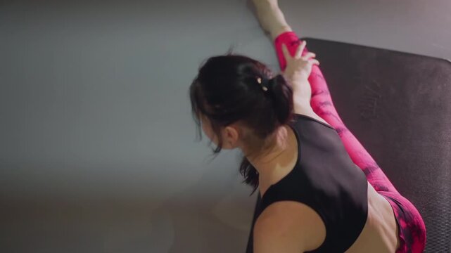 female athlete stretching leg on mat seated hamstring reach high leg extension pink leggings black crop top overhead view precise mobility work dynamic warmup for dance or pilates steady breath