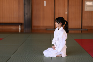 道場で正座をして真っ直ぐ前を見つめる空手着の少女　武道の礼儀と精神統一