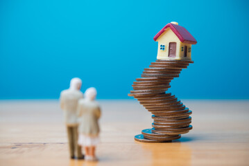 Senior couple looking at house on unstable stack coins. Financial risk management for retirement, mortgage loan, asset forfeiture, bankruptcy, reverse mortgage, financial literacy and so on concept.