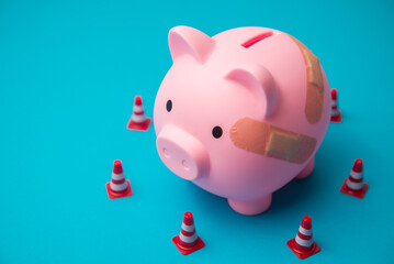 Injured piggy bank and traffic cones on blue background. Personal financial problem from high interest rate loan, loss investment, high cost, economy crisis, etc. effect to savings and so on concept.