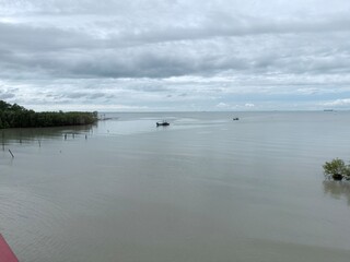 Naklejka premium Calm coastal shoreline with rocks, shallow sea, and cloudy sky, representing natural seascape, coastal environment, peaceful waters, and outdoor landscape scenery.
