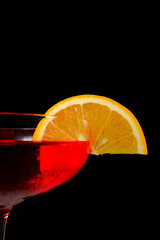 Vibrant close up shot featuring a bright red cocktail garnished with a fresh, juicy orange citrus slice against a black background © The Prince 