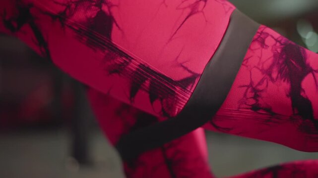 female trainer in pink leggings using band looped around thigh during banded hip abduction, gym background, focused coach demonstration, rhythmic controlled reps, emphasis on glute activation and form