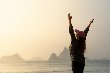 Fototapeta premium Woman Raising Arms at Sunrise by the Sea with Mountains
