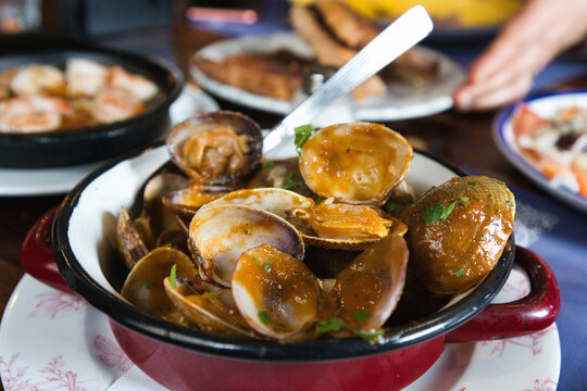 Appetizing seafood clams served in a rustic red enamel pot, seasoned with herbs and sauce, creating a delicious culinary experience on a restaurant table