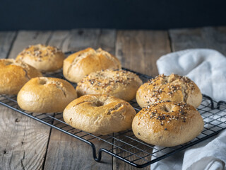 Top view of freshly made homemade bagels sprinkled with seeds on a cooling rack on a rustic table
