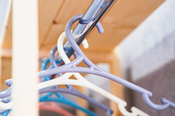 A close-up of a row of plastic coat hangers in pastel shades (beige, grey, white, peach) hanging neatly on a metal rod. Soft lighting creates a warm, minimalist atmosphere.