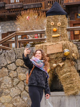 in the traditional Sauris mountain Carnival, A smiling woman takes a selfie with a straw figure decorated with an orange and corn. Sauris,Friuli Venezia Giulia,Italy