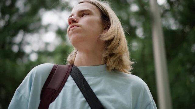 young caucasian guitarist gazing at sky in low angle park shots with guitar case backpacked, confident posture, busking vibe, urban green canopy, cinematic movement between frames, stride toward city,