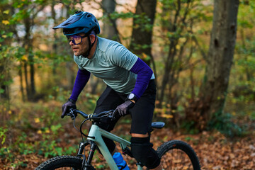 Fototapeta premium Focused Mountain Biker Riding Through Forest Trail in Gear, Helmet, Gloves, and Knee Pads