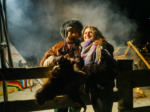 During the carnival procession, of Sauris, A smiling woman embraces a man in a traditional mask and fur costume at night. Sauris,Friuli Venezia Giulia,Italy