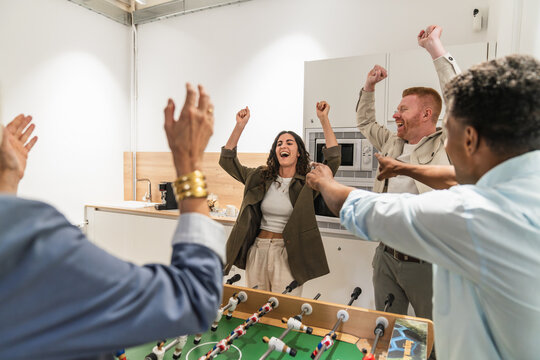 Multiracial office workers celebrating winning a competitive foosball game in the employee break room, fostering teamwork and fun