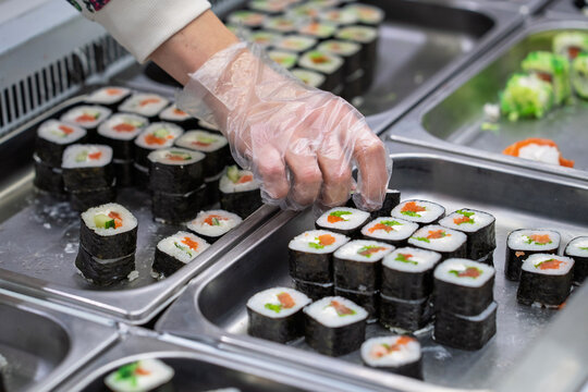 Buying sushi rolls in a store. A customer's hand in a disposable glove selects sushi rolls in a store.
