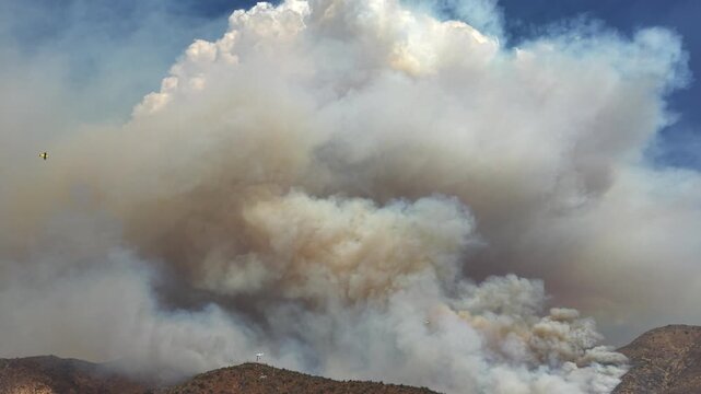 Majestic aerial drone shot of a colossal pyrocumulus smoke plume rising from a wildfire, towering over a firefighting helicopter flying alongside it for scale in Chile and 4k