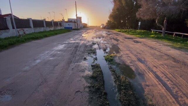 Flooded stream flows through green coastal vegetation after heavy rain near the beach Mud tracks and rain puddles reflect soft morning light on a sandy coastal access road after rainfall