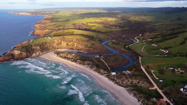 A wide golden hour aerial over Snelling Beach and the Middle River estuary, with rolling green hills and the lush coastal landscape of Kangaroo Island, Australia in the distance.