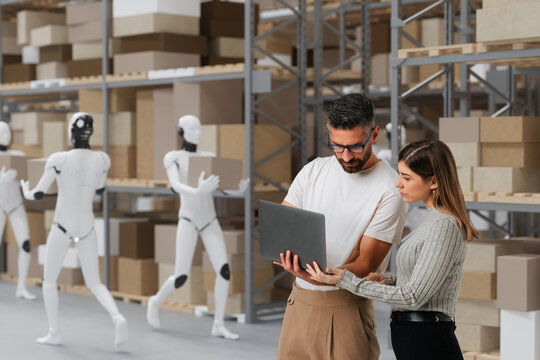 Logistics team reviewing warehouse data while humanoid robots move inventory