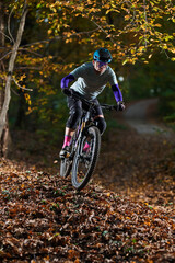Fototapeta premium Autumn Mountain Biker Riding Through Leafy Forest Trail on a Scenic Fall Day