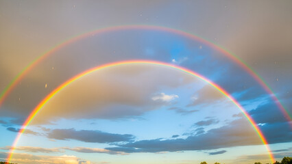 Vibrant double rainbow in blue sky with clouds