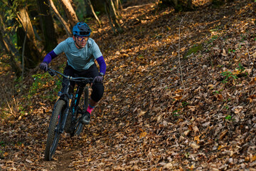Male Mountain Biker Riding Through Forest Trail on Leaf-Littered Path in Autumn