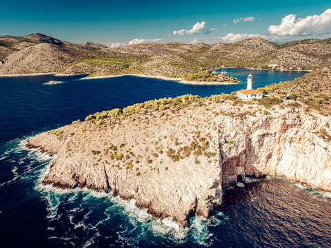 Aerial view of a stark white lighthouse standing sentinel on a rugged cliff against the deep blue sea, contrasting with the arid landscape, Lastovo, Dubrovnik-Neretva County, Croatia.