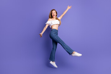 Joyful young woman in trendy attire posing against vibrant violet background and radiating...