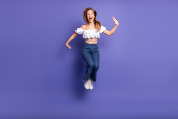 Joyful young woman in casual summer attire jumping with excitement against a vibrant purple...