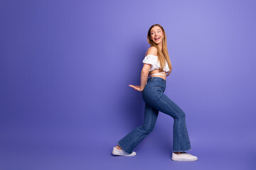 Cheerful young woman posing stylishly in a trendy outfit against a vibrant purple background for...