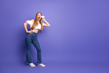 Charming Woman with Surprised Expression Holding Toy Phone Against Purple Background Wearing Casual...