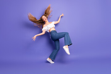 Charming young woman in trendy outfit jumping joyfully against a vibrant violet background...