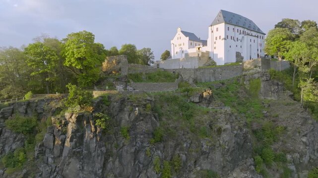 Spectacular aerial view of Wolkenstein Castle, perched on a steep rocky outcrop above the Zschopau Valley. The image shows the striking white castle complex and the adjacent town of Wolkenstein.