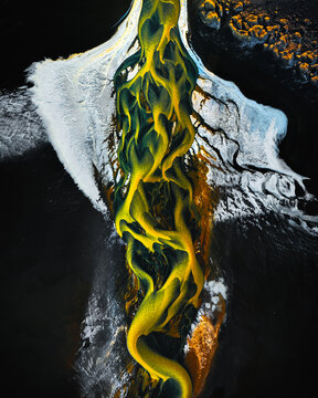 Aerial view of glacial rivers cut through the black sands, a tapestry of gold and white against the stark landscape, Iceland.