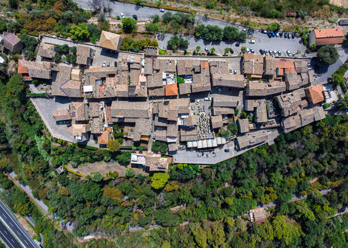 Aerial view of a compact medieval village with terracotta rooftops nestled amidst verdant hills, Torre di Palme, Marche, Italy.