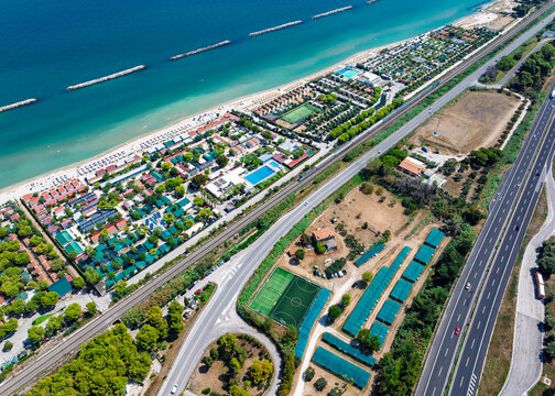 Aerial view of the coastline where turquoise waters meet golden sands, and roads run parallel to the sea, Torre di Palme, Marche, Italy.