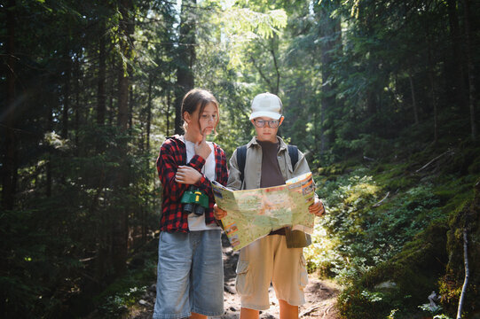 Children tourists hiking and reading map in forest