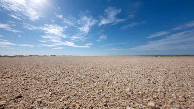 Expansive arid landscape with gravel ground under a bright blue sky with sun and clouds