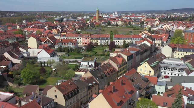 View over the UNESCO World Heritage old town of Bamberg. The characteristic red tiled roofs and historic streets stretch out in front of the forested hills of the Steigerwald under a clear spring sky.