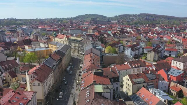 View over the UNESCO World Heritage old town of Bamberg. The characteristic red tiled roofs and historic streets stretch out in front of the forested hills of the Steigerwald under a clear spring sky.
