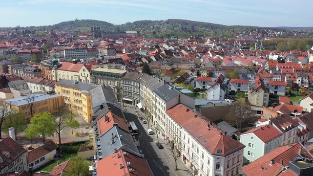 View over the UNESCO World Heritage old town of Bamberg. The characteristic red tiled roofs and historic streets stretch out in front of the forested hills of the Steigerwald under a clear spring sky.
