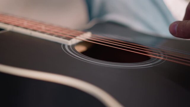 closeup acoustic guitar string detail gentle finger picking on black gloss body, light blue sleeve visible, soft natural lighting, warm timbre and subtle resonance, studio practice vibe, focused