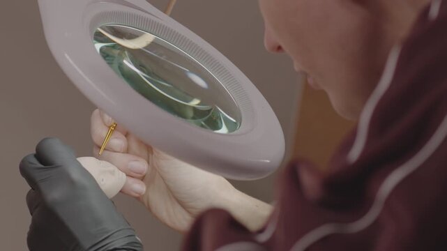 Gloved artist painting silicone doll face under magnifying glass, focusing on precision work and capturing fine features in handcrafted miniature figure