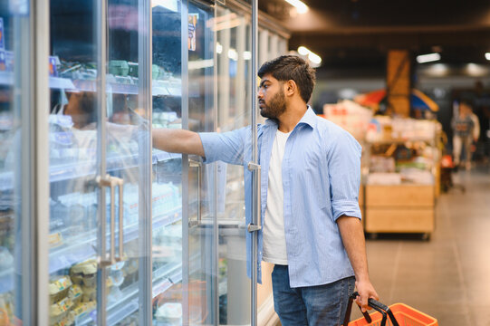 Young indian man choosing frozen food in supermarket refrigerator
