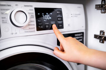 Naklejka premium Finger touches digital sensor on washing machine display panel. Close up of modern white appliance for laundry routine. Household technology and smart home chores concept
