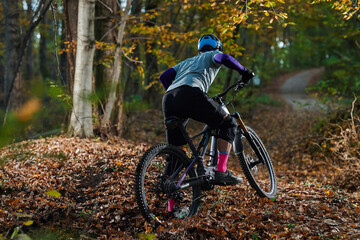 Fototapeta premium Mountain Biker in Autumn Forest Navigating Leaf-Covered Trail on a Rugged Path During Colorful Fall Sunlight