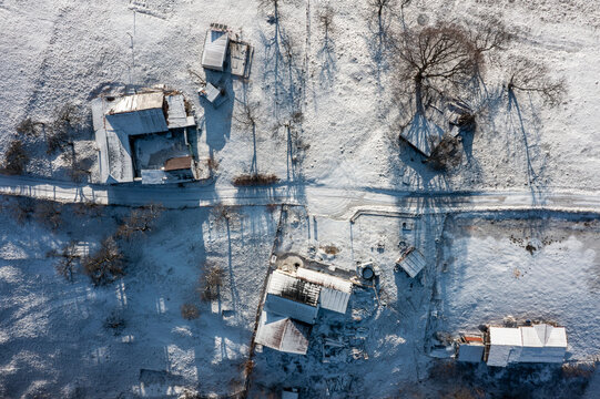 Aerial view of snow-dusted rooftops and frosted fields create a serene winter tableau in the Romanian countryside, Holbav, Brasov, Romania.