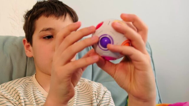 Focused boy holds a colorful puzzle ball close to his face, tight portrait framing with soft home light. Tactile play supports attention skills and offers a screen free way to calm the mind.