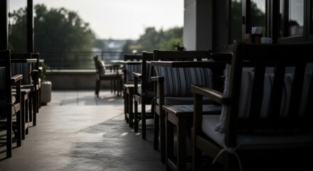 Fototapeta premium Outdoor dining area with wooden chairs and striped cushions, overlooking a blurred landscape